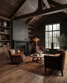 A rustic, cozy living room with dark wood ceiling beams, a black fireplace, leather armchairs, a round wooden coffee table, and a large patterned area rug on a hardwood floor. Rustic Modern Floor lamp rattan shade with terracotta stone base wabi sabi